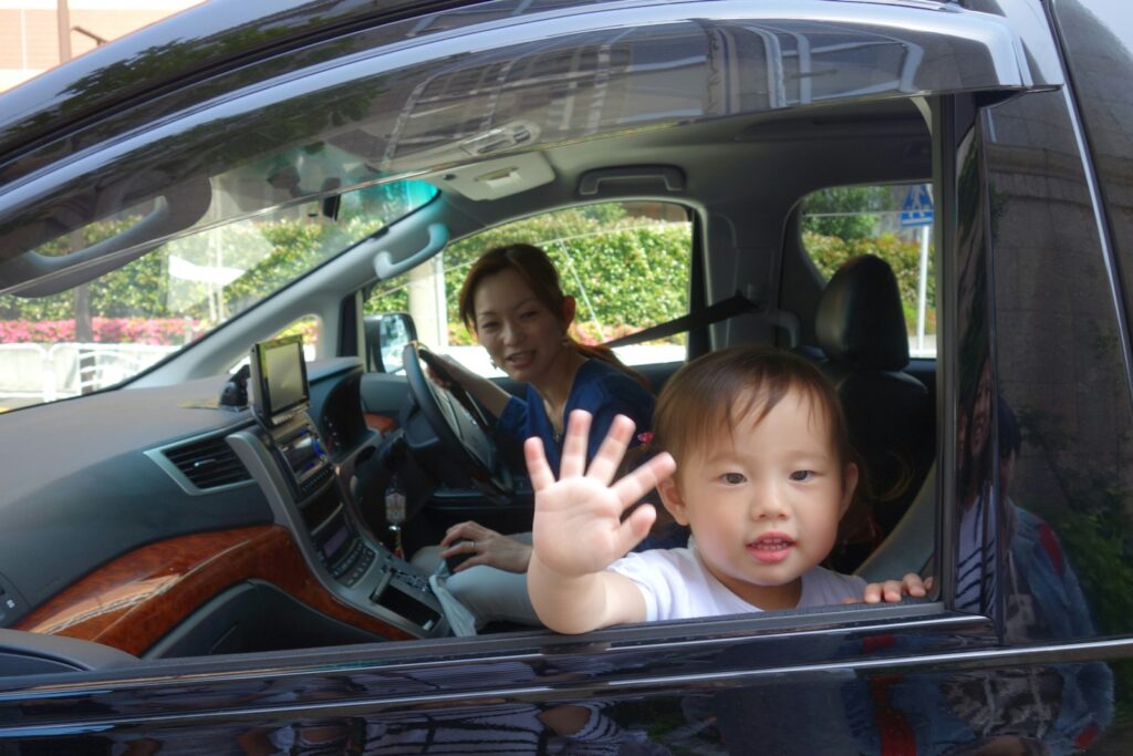 When Can Kids Sit in the Front Seat: Child Passenger Safety Laws and Guidelines Child waves from car window with mother driving