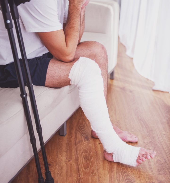 A man with crutches and a leg cast sitting on a couch
